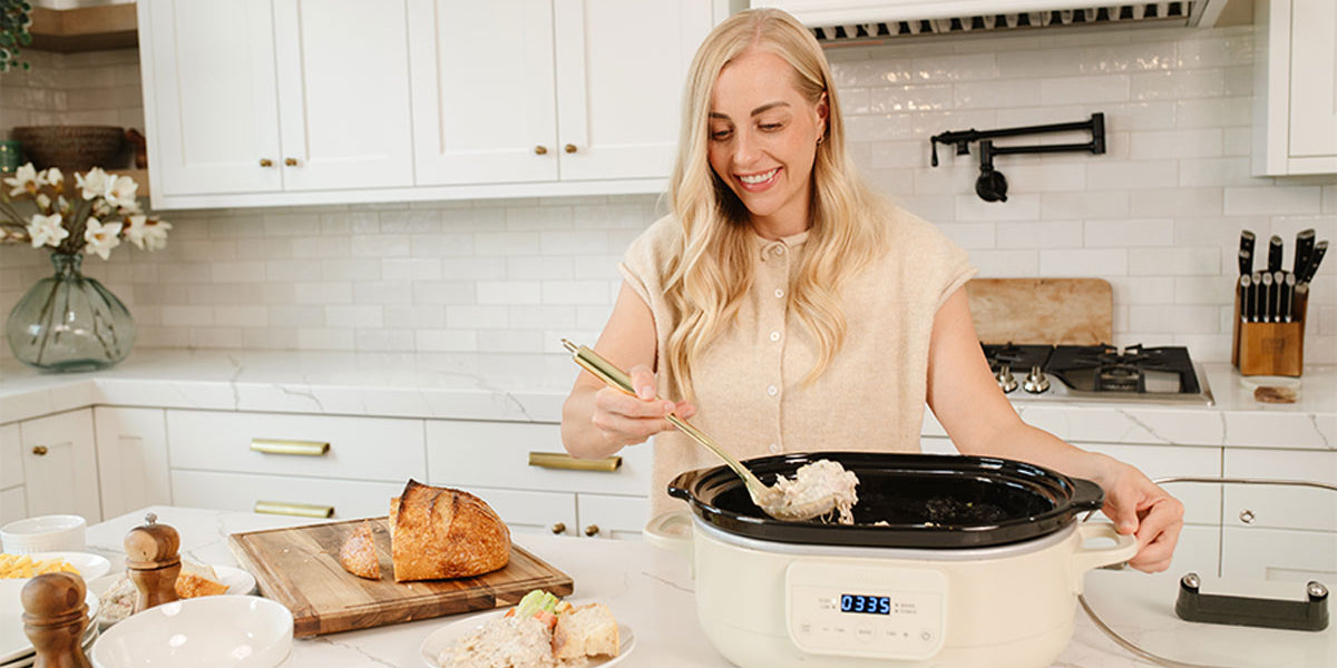 Woman scooping shredded chicken mixture out of slow cooker onto a plate in a white kitchen.