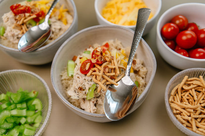 Gray bowl with shredded chicken, crunch noodles, tomatoes and celery with a silver spoon.