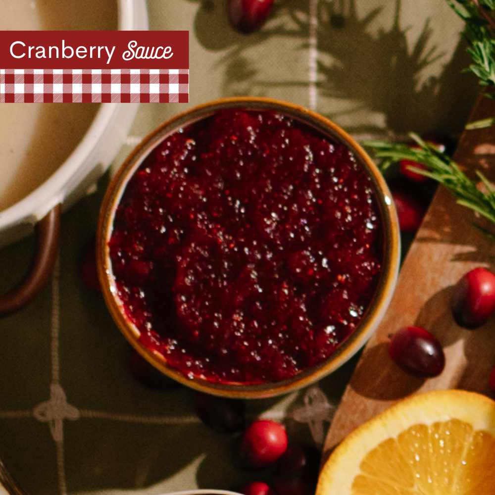 A small dish of Cranberry Sauce on top of a green plaid table cloth with A red-and-white gingham banner at the top left reads 'Cranberry Sauce'.