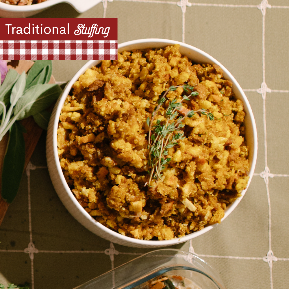 Stuffing in a white bowl with herbs on top on a green plaid table cloth with A red-and-white gingham banner at the top left reads 'Traditional Stuffing'.
