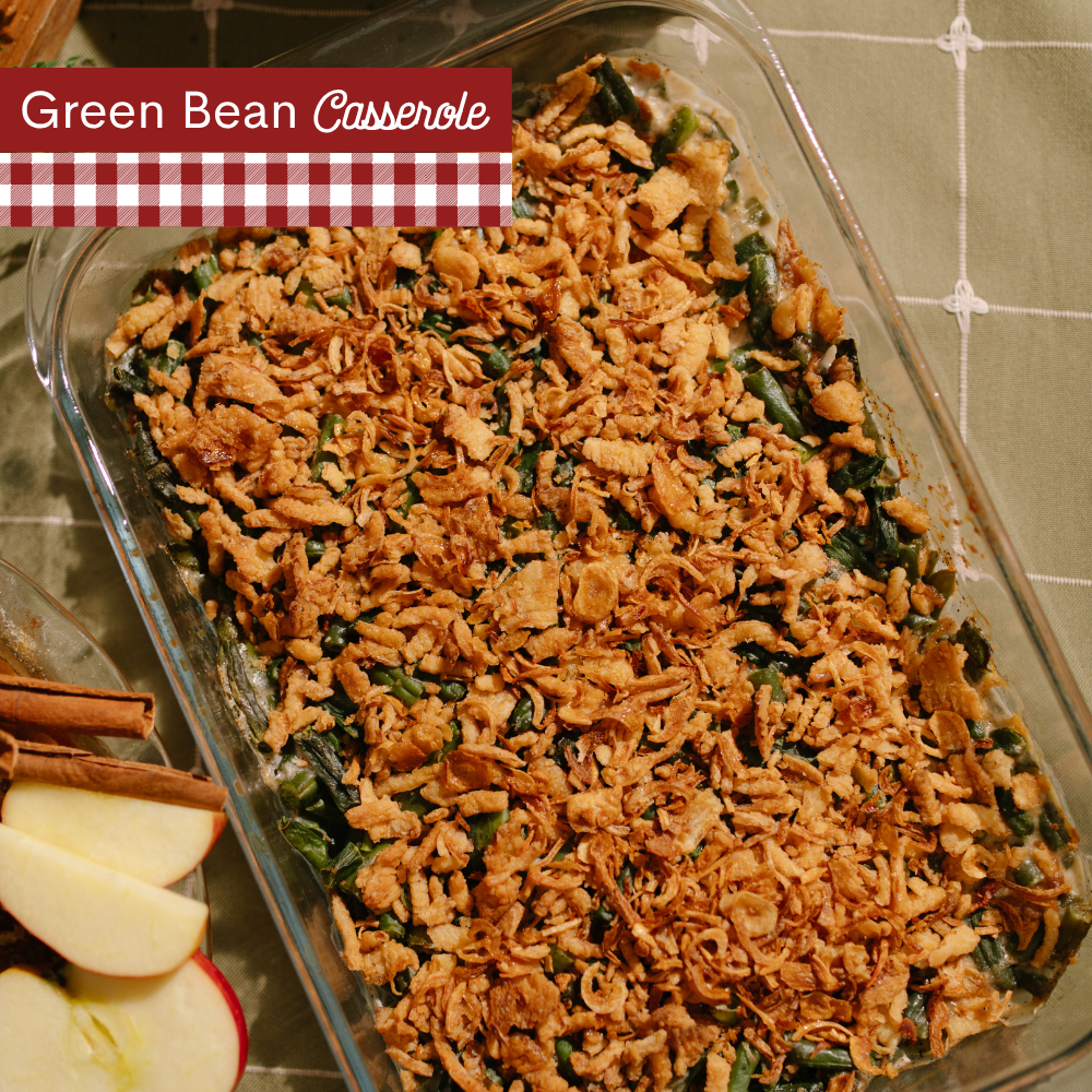 A glass baking dish filled with green bean casserole topped with a golden brown crispy fried crumb mixture, photographed from above on a tiled surface. A red-and-white gingham banner at the top left reads 'Green Bean Casserole.