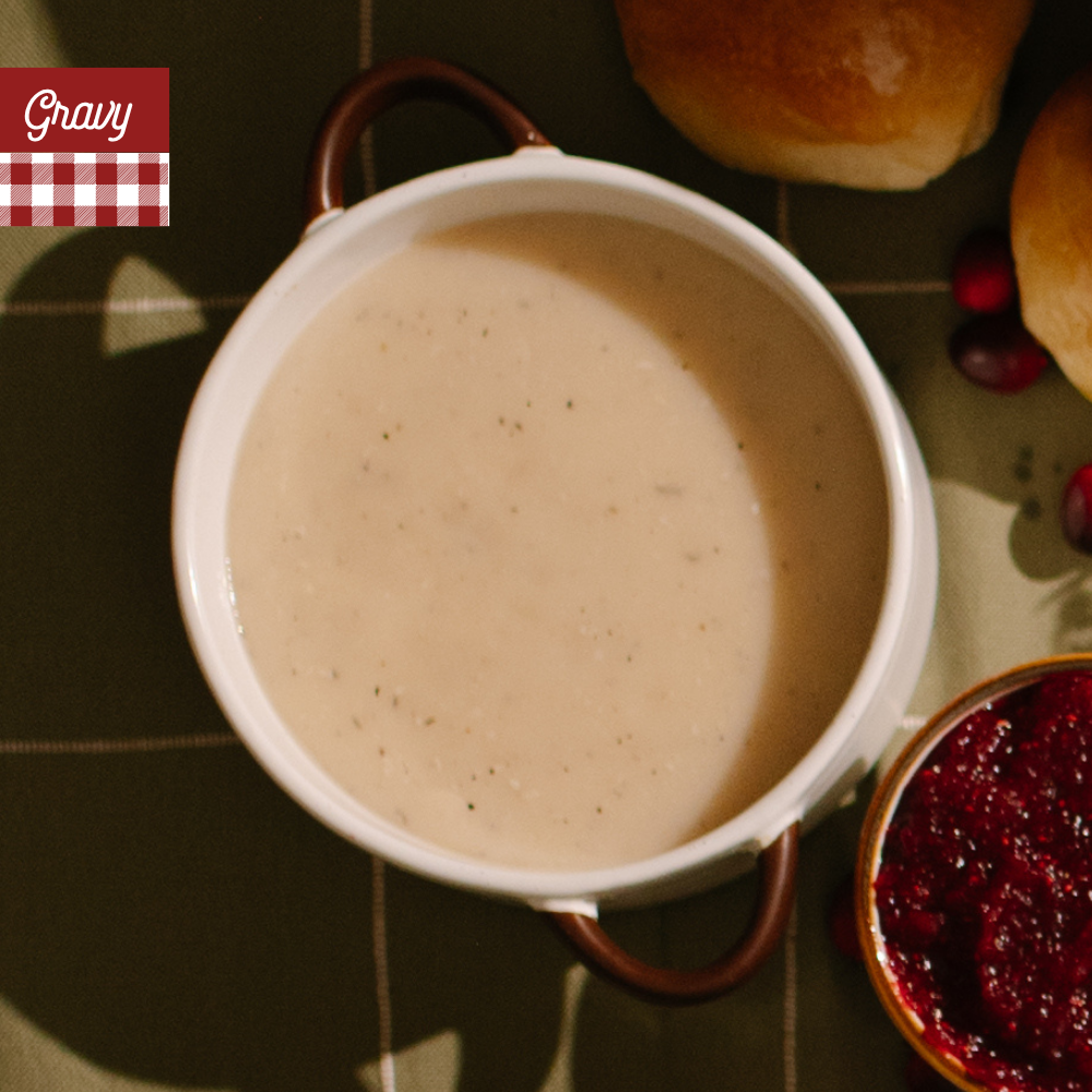 White gravy in a small white dish on a green plaid table cloth with A red-and-white gingham banner at the top left reads 'Gravy'.