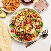 BBQ chicken salad in a bowl with toppings on a white surface