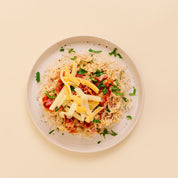 A top-down view of a plated food dish on a light beige background. The dish consists of a bed of white rice topped with shredded Bacon Chicken Ranch, shredded yellow cheese, diced red tomatoes, and chopped green herbs, served on a round off-white plate.