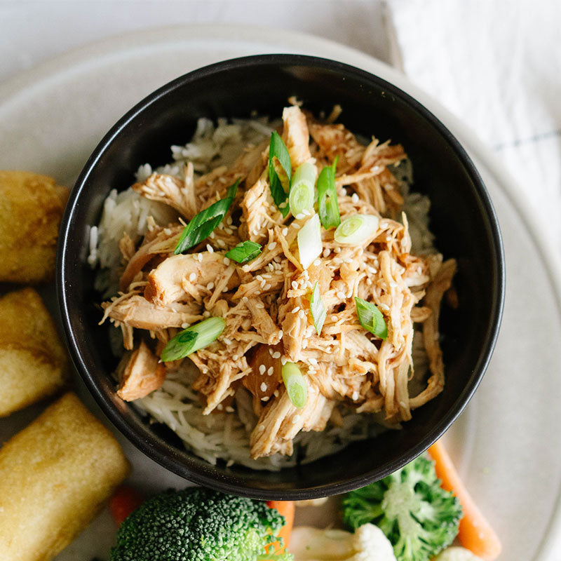 Bowl of shredded chicken with green onions on a plate with egg rolls and vegetables