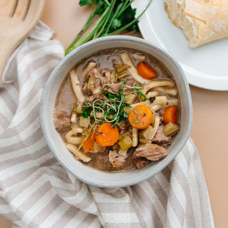 Bowl of soup with noodles, carrots, and herbs on a striped cloth