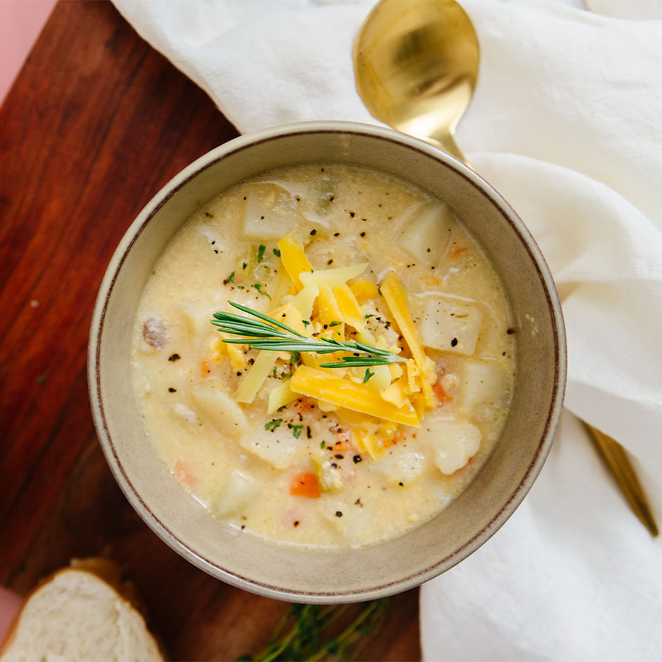 Bowl of potato soup topped with shredded cheese on a wooden background.