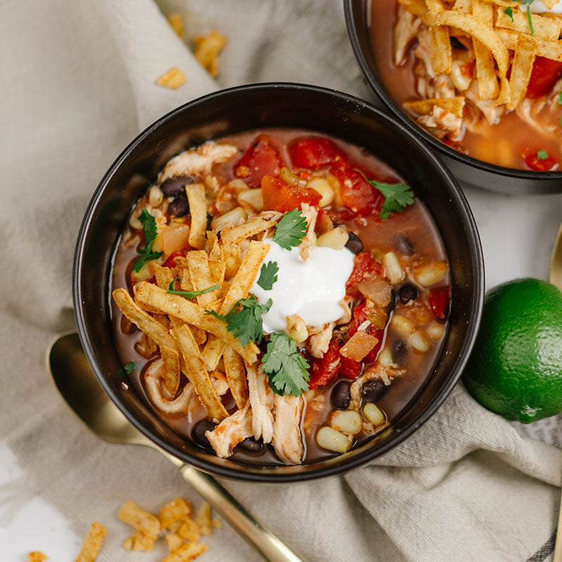 Bowl of chicken enchilada soup with toppings on a beige cloth