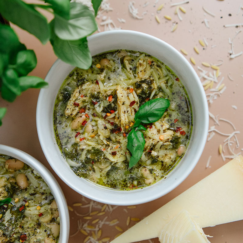 Pesto pasta dish in a white bowl with basil leaves on a pink background