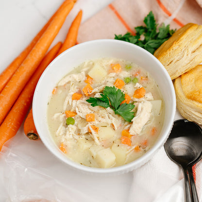 Bowl of chicken soup with carrots, a biscuit, and parsley on a white background
