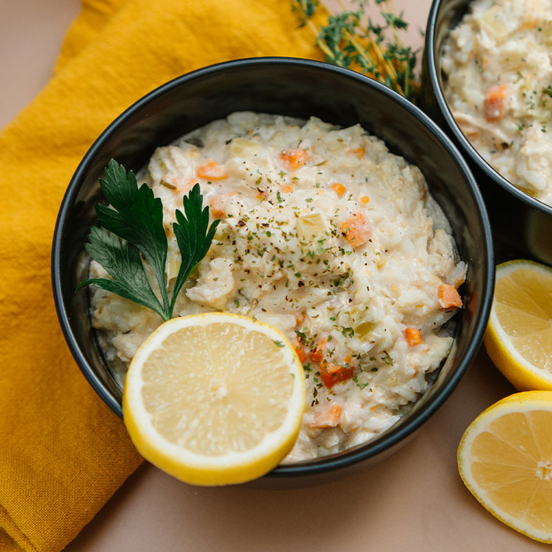 Bowl of creamy rice soup with lemon slices and parsley on a yellow cloth.