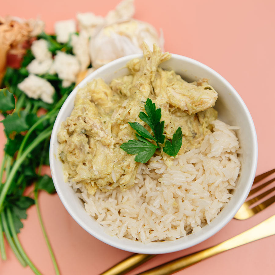 White bowl with Beehive Meals Chicken and Stuffing and rice on a pink background with a gold fork and knife.