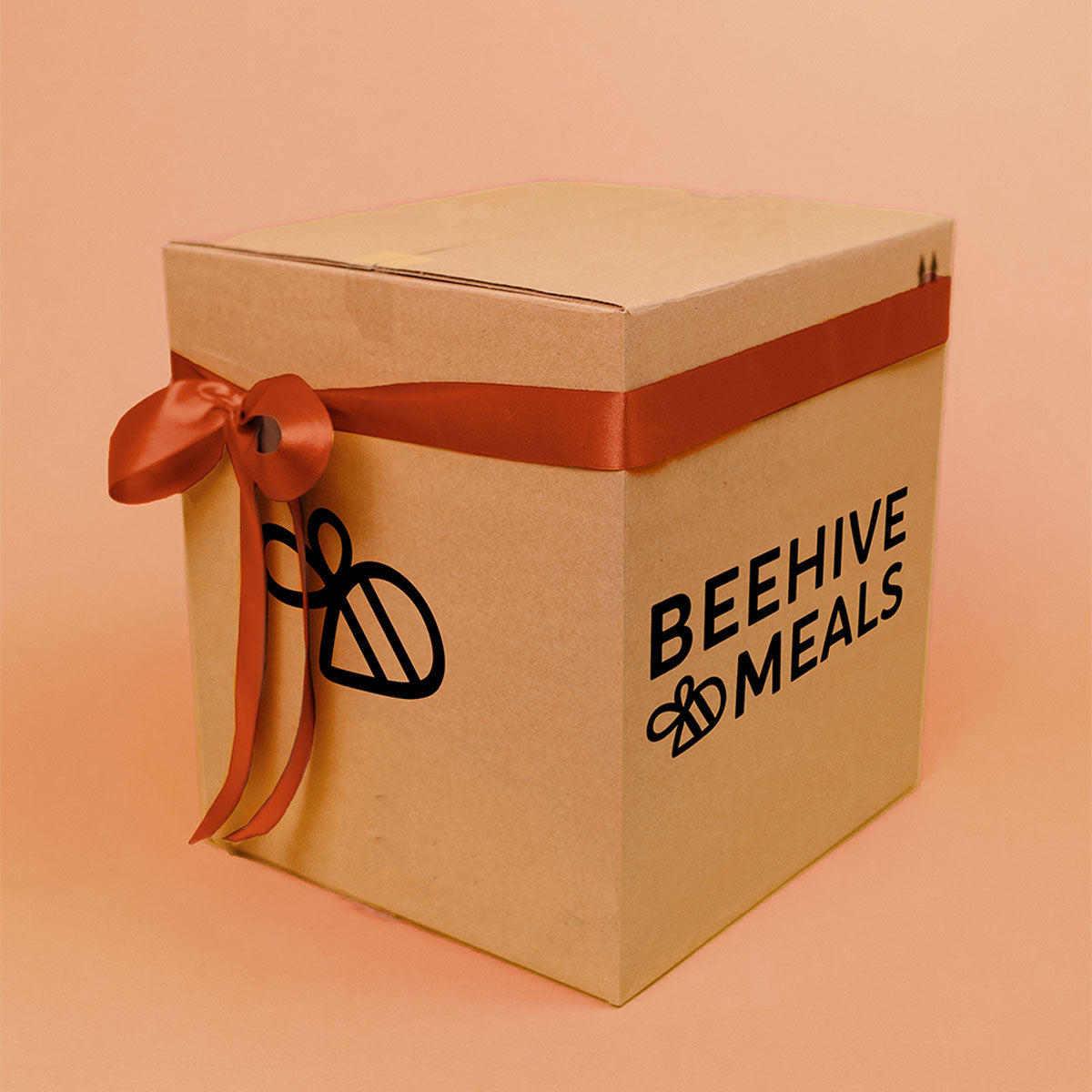 Cardboard box with a red ribbon and 'Beehive Meals' logo on a peach background