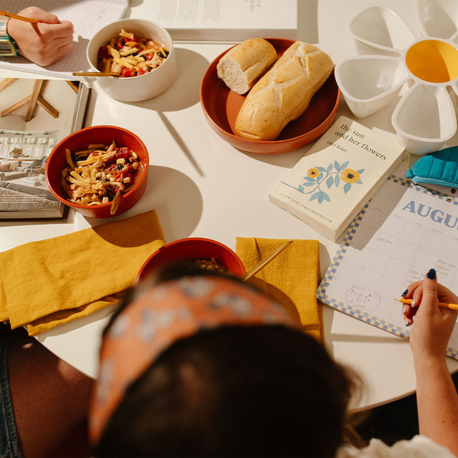 People sitting at a table with food, books, and a calendar.