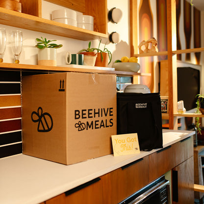 Beehive Meals box and black bag on a kitchen counter with shelves in the background.