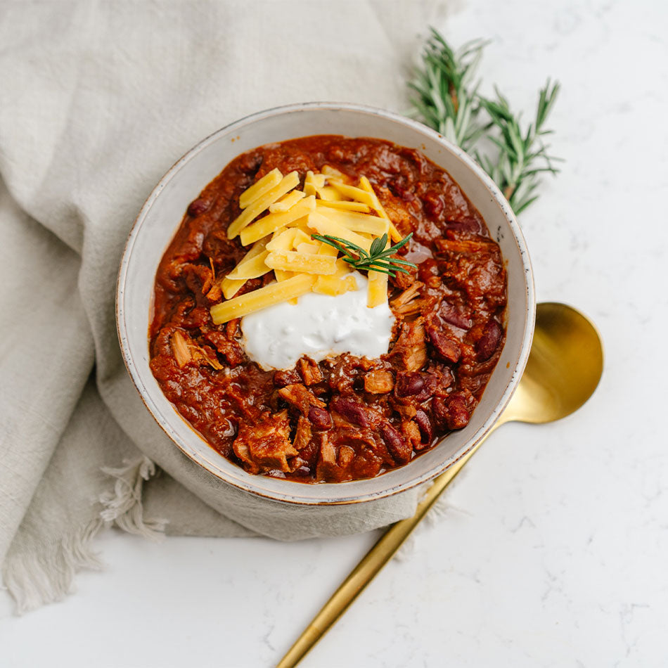 Bowl of chili with cheese and sour cream on a white surface