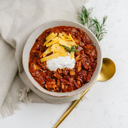 Bowl of chili with cheese and sour cream on a white surface
