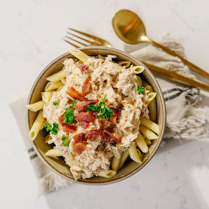 Bowl of Beehive Meals Bacon Chicken Ranch pasta on a marble surface with a golden fork and spoon.
