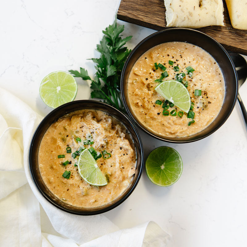 Two bowls of soup with lime wedges and herbs on a white surface