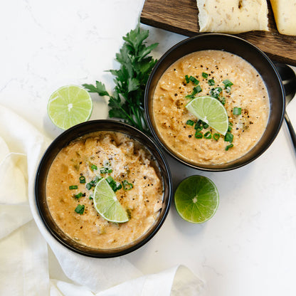 Two bowls of soup with lime wedges and herbs on a white surface