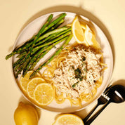 Plate of shredded chicken and pasta with lemon and asparagus on a beige background