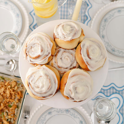 Plate of cinnamon rolls with white frosting on a table setting with plates and glasses.