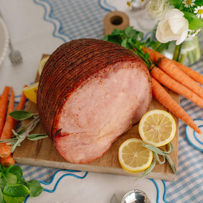 Smoked ham on a wooden board with lemons and carrots on a decorative tablecloth.