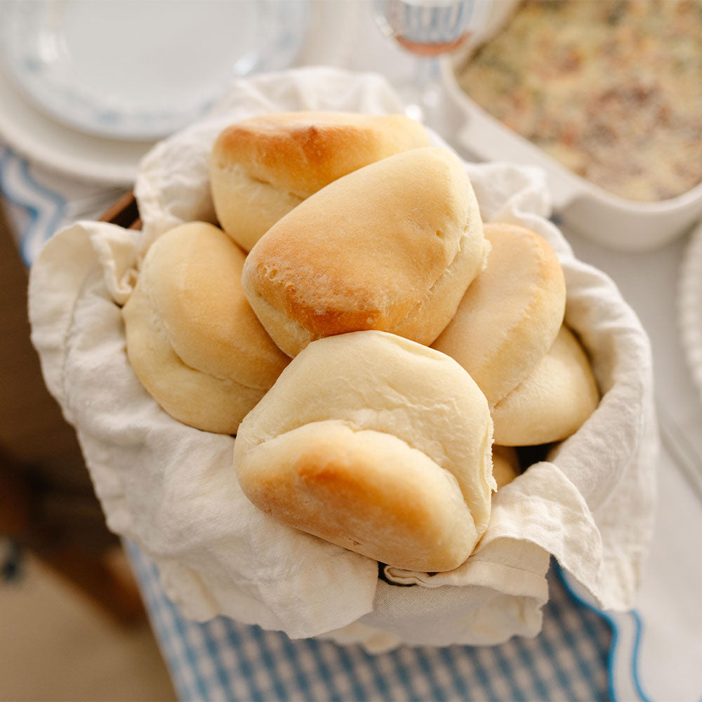 Dinner rolls in a basket with a white cloth on a blurred background