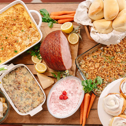 Assorted holiday dishes including a ham, carrots, and various casseroles on a wooden table.