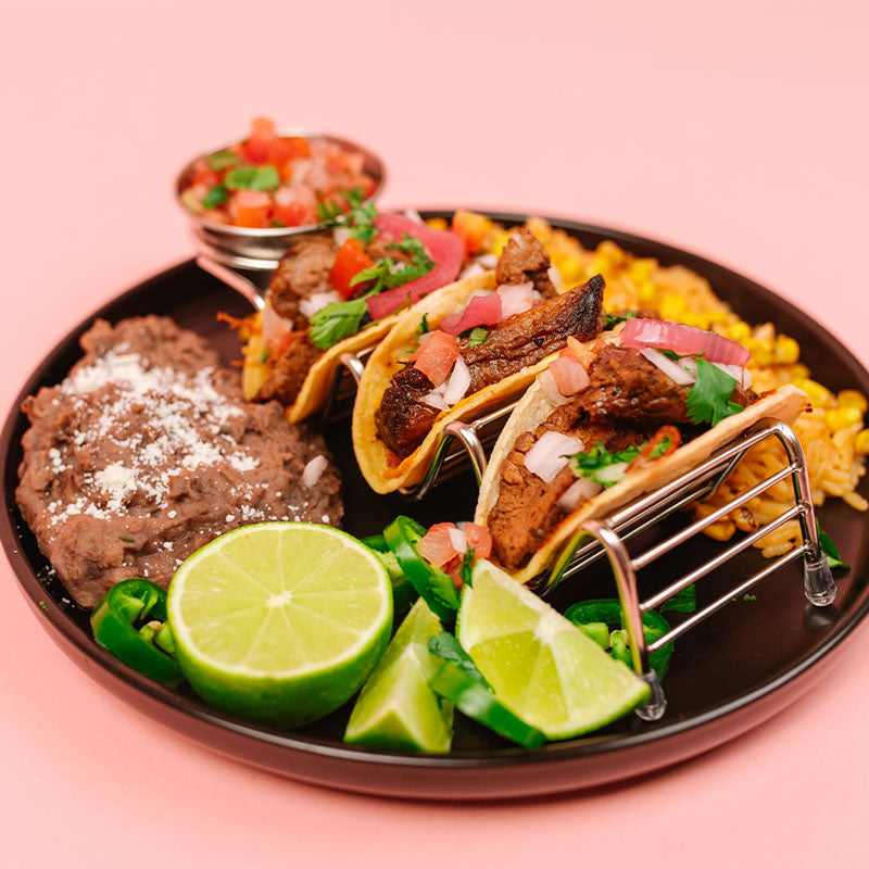 Platter of tacos with lime wedges on a pink background