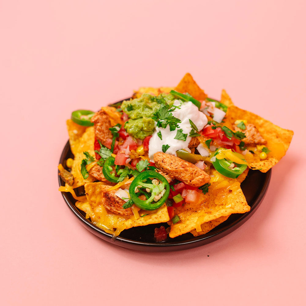 Plate of nachos with various toppings on a pink background