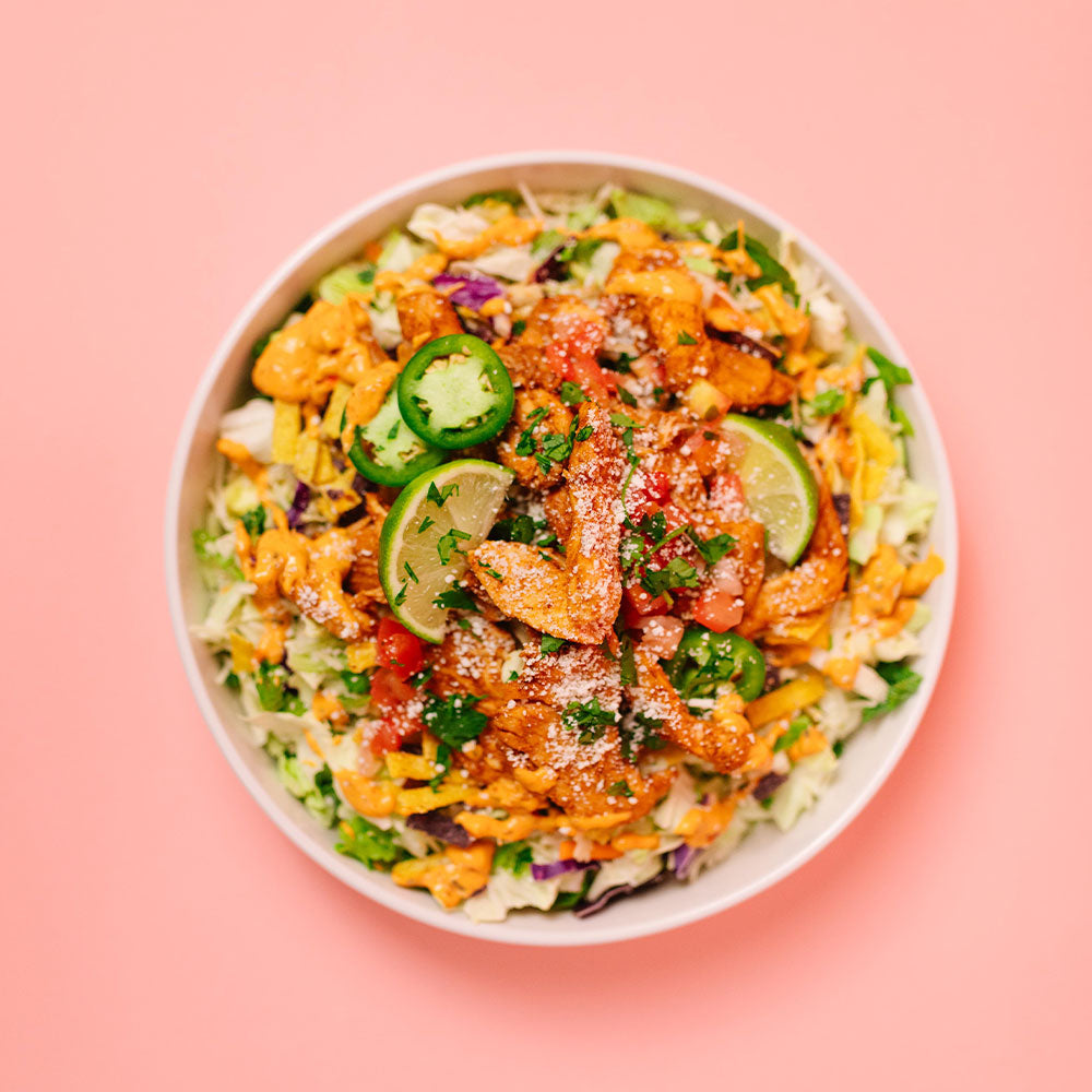 Colorful salad with chicken, lime, and cheese in a white bowl on a pink background