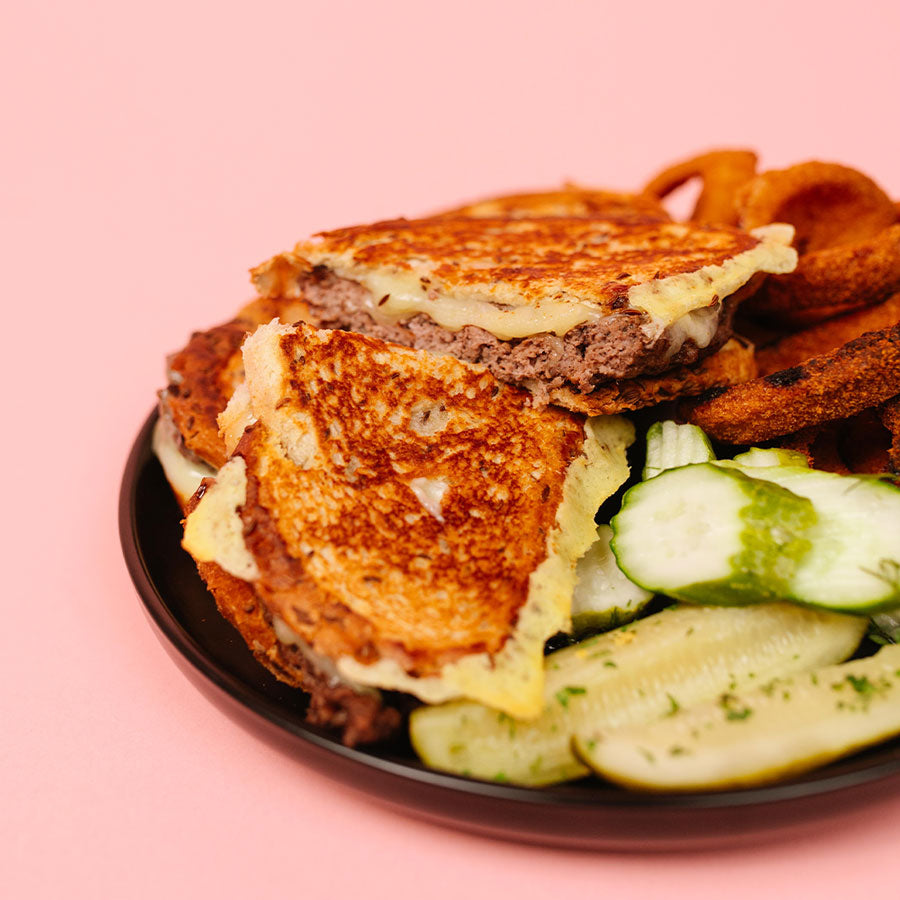 Grilled patty melt sandwich with pickles on a pink background