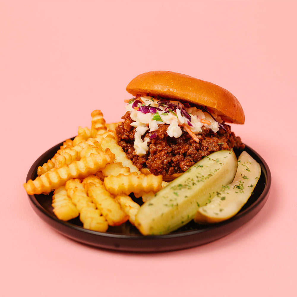 Sloppy Joes with fries and pickles on a pink background