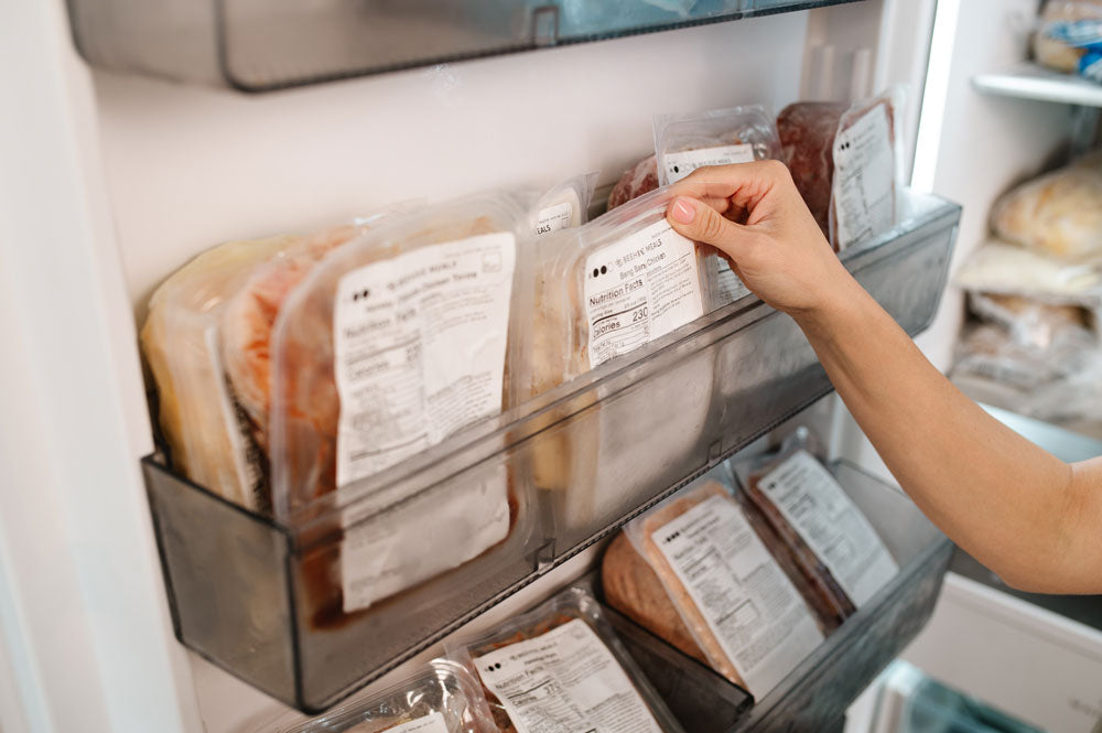 A hand reaching for a Beehive Meal from a freezer door shelf. 