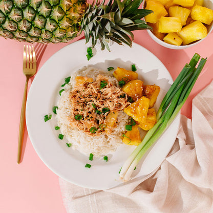 Beehive Meals Hawaiian Teriyaki Chicken over rice with pineapple and green onions on the side on a pink background