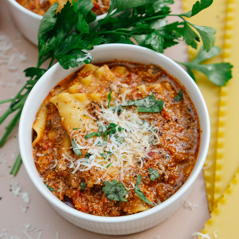 Bowl of lasagna soup with parmesan cheese on a light background