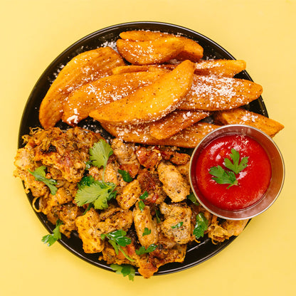 A top-down view of a black plate filled with golden-brown sweet potato wedges dusted with powdered sugar, seasoned chicken and rice, and a small metal cup of ketchup on a solid yellow background.