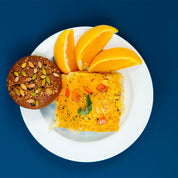 Breakfast casserole on a white plate with orange slices and a muffin against a blue background