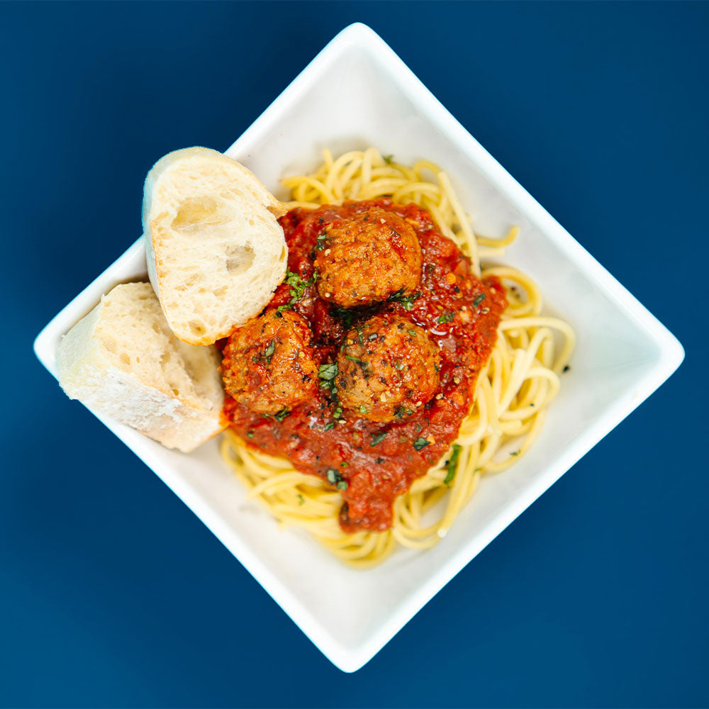 Spaghetti with meatballs and bread on a white plate against a blue background