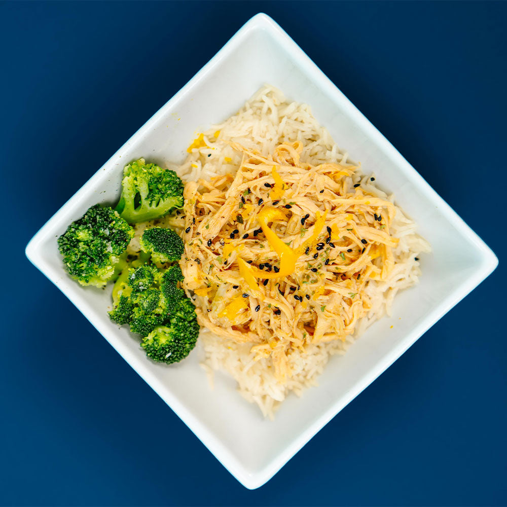 White plate with rice and chicken with a side of broccoli on a blue background