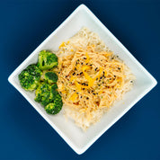 White plate with rice and chicken with a side of broccoli on a blue background