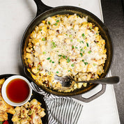 Eggs bacon and potatoes in a black skillet with a silver spoon.