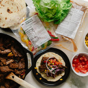 Prepared steak fajita ingredients and a taco on a marble surface with visible labels.