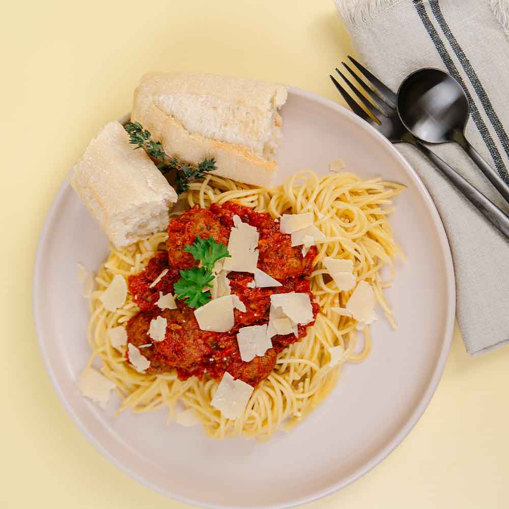 Plate of spaghetti with meat sauce, bread, and a sprig of thyme on a yellow background.