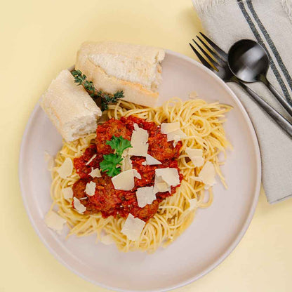 Plate of spaghetti with meat sauce, bread, and a sprig of thyme on a yellow background.