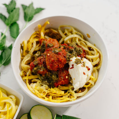 Bowl of spaghetti with tomato sauce, herbs, and a dollop of ricotta cheese on a white background