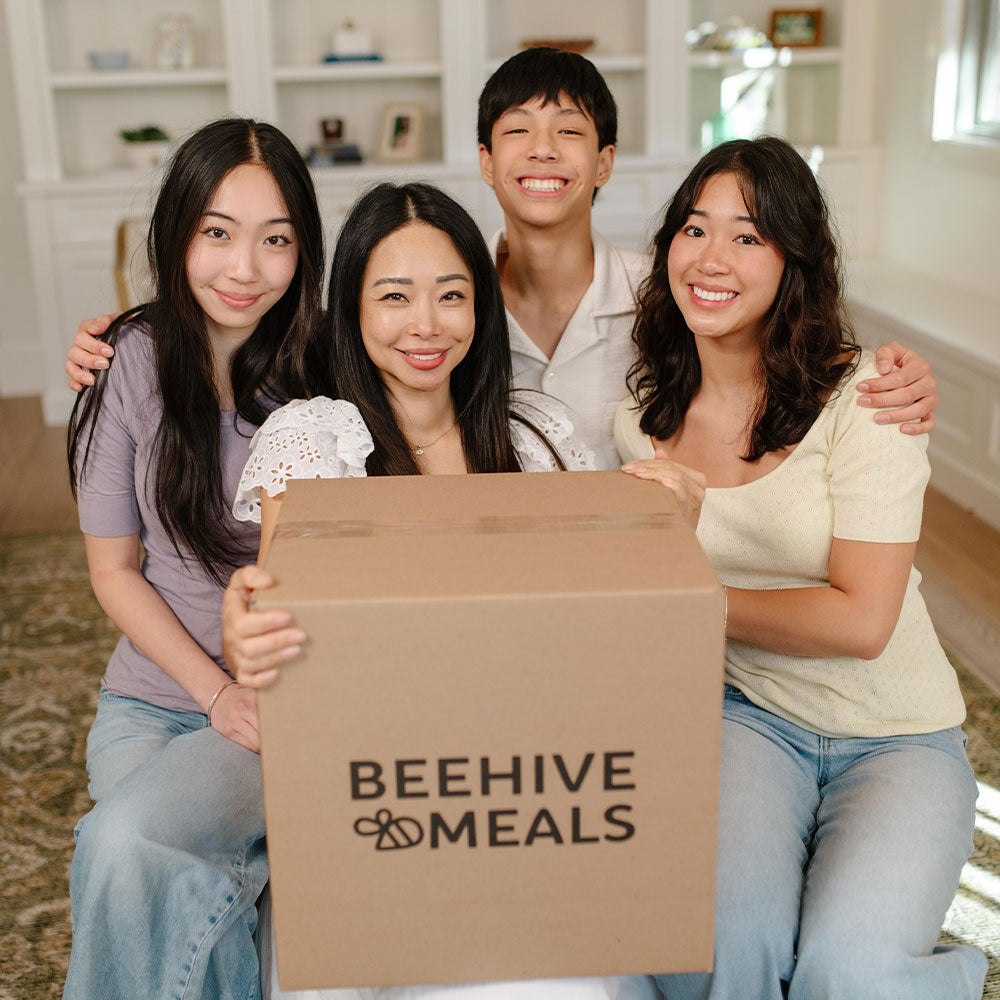 Four people holding a box with 'Beehive Meals' logo in a home setting