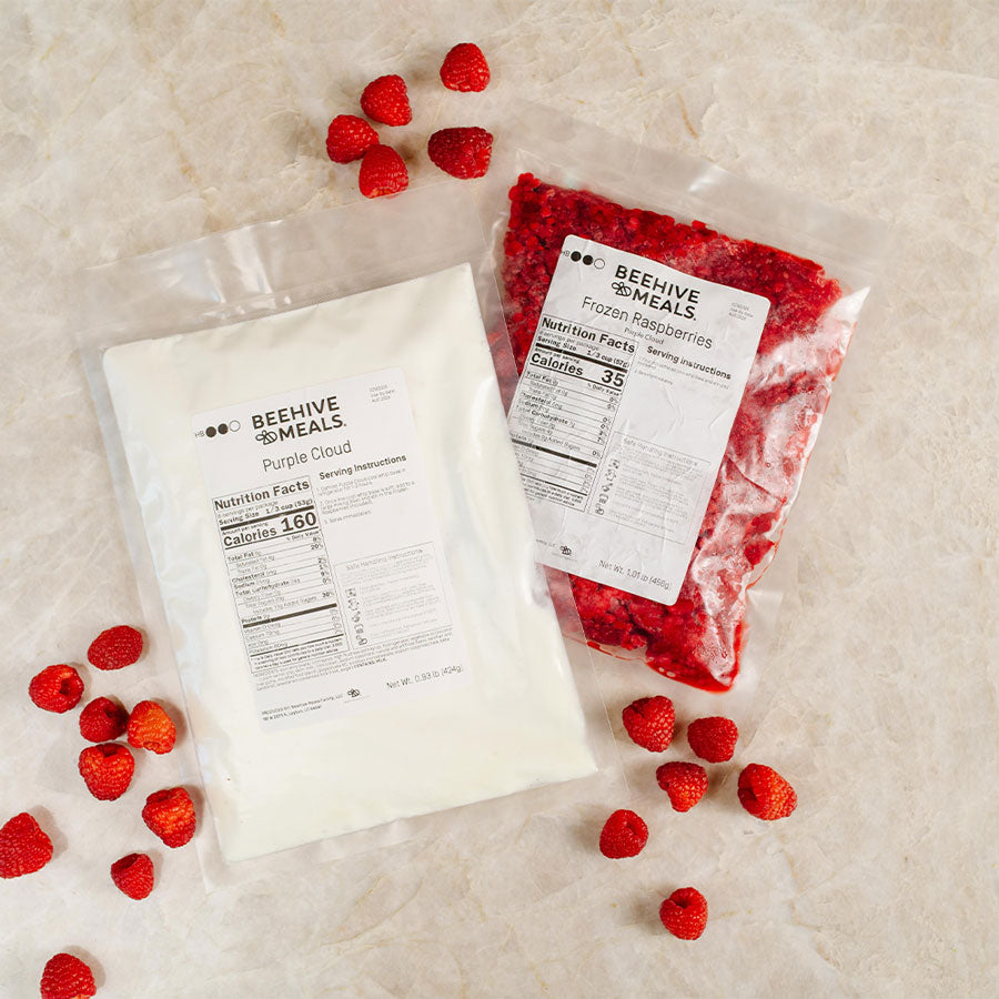 Two packages of Beehive Meals with frozen raspberries on a light surface