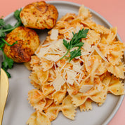 Plate of Beehive Meals Sausage Alfredo with bow tie pasta with herbs and bread on a pink background.